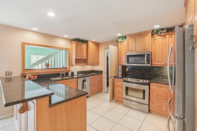 kitchen featuring light tile patterned floors, decorative backsplash, appliances with stainless steel finishes, dark stone countertops, and a peninsula