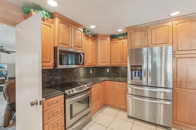 kitchen with light tile patterned floors, appliances with stainless steel finishes, dark stone counters, and backsplash