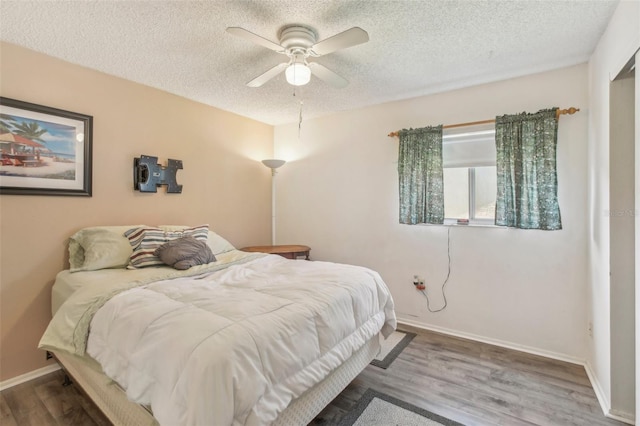 bedroom featuring ceiling fan, a textured ceiling, baseboards, and wood finished floors