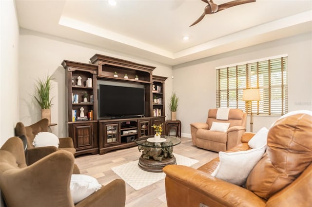 living room with baseboards, recessed lighting, ceiling fan, light wood-style floors, and a raised ceiling