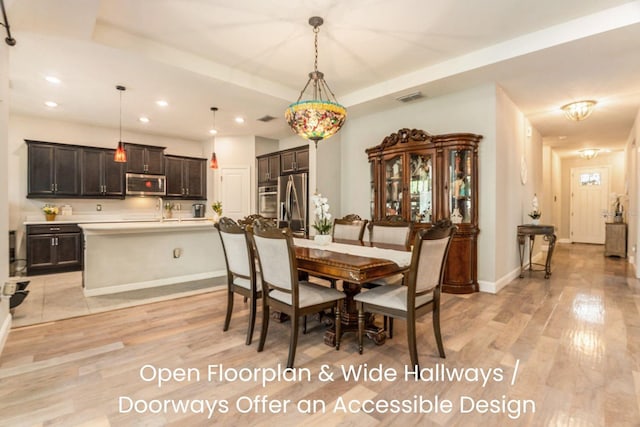 dining space with baseboards, visible vents, light wood-style flooring, recessed lighting, and a raised ceiling