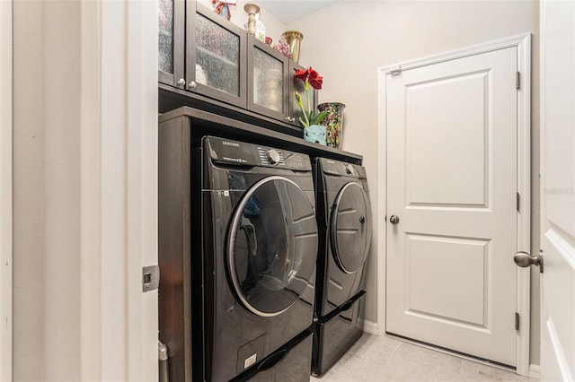 laundry area featuring light tile patterned flooring, cabinet space, and washer and clothes dryer