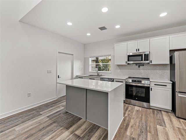 kitchen with light wood finished floors, white cabinetry, stainless steel appliances, and a sink