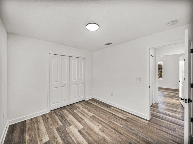 unfurnished bedroom with a closet, visible vents, baseboards, and wood finished floors