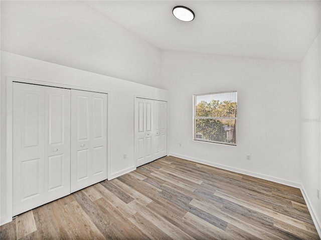 unfurnished bedroom with baseboards, multiple closets, lofted ceiling, and wood finished floors