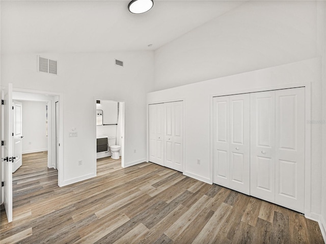 unfurnished bedroom with visible vents, baseboards, multiple closets, wood finished floors, and high vaulted ceiling