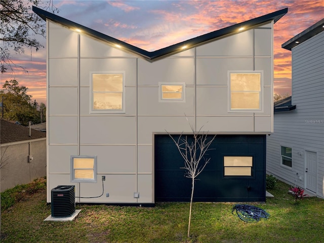 back of property at dusk with central air condition unit, a lawn, and stucco siding