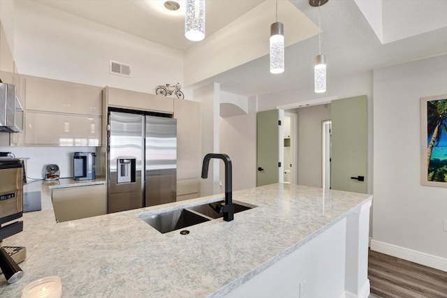 kitchen with visible vents, hanging light fixtures, light stone countertops, stainless steel refrigerator with ice dispenser, and a sink