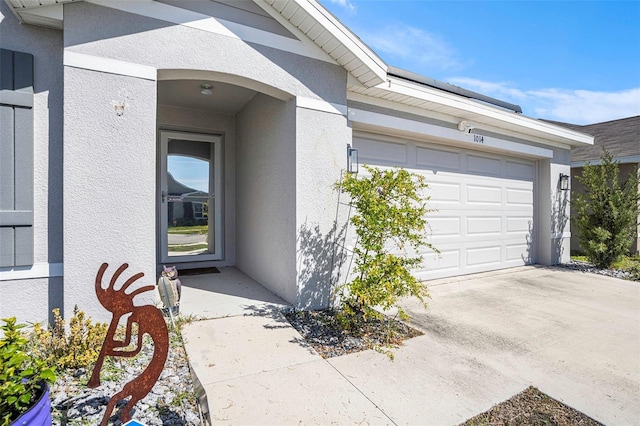 doorway to property with a garage, concrete driveway, and stucco siding