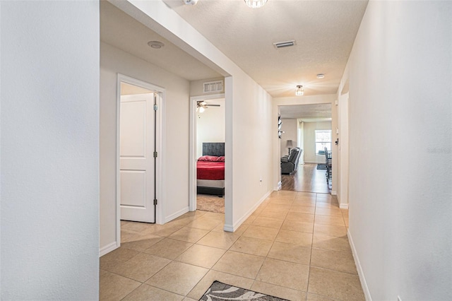 corridor featuring light tile patterned floors, a textured ceiling, visible vents, and baseboards