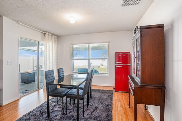 dining area with a textured ceiling, wood finished floors, visible vents, and baseboards