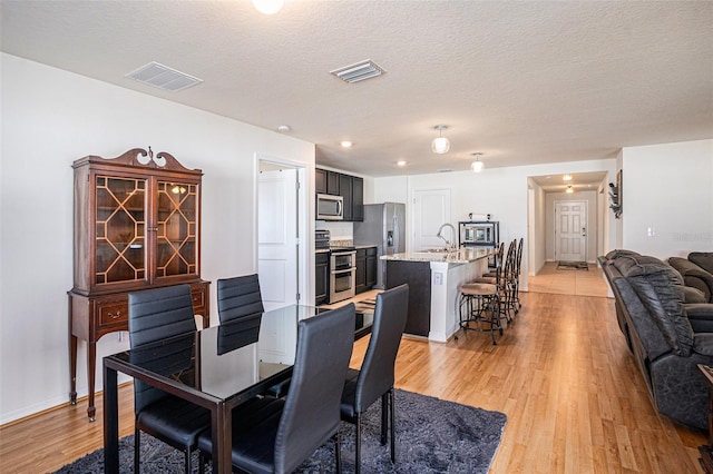 dining room featuring a textured ceiling, light wood-style flooring, and visible vents