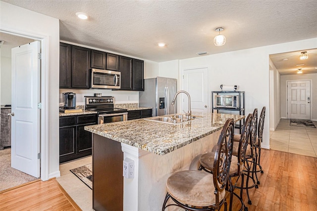 kitchen featuring light wood finished floors, appliances with stainless steel finishes, a sink, an island with sink, and a kitchen breakfast bar