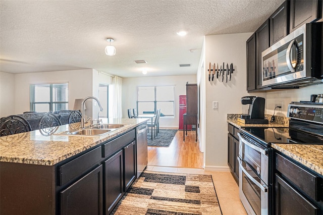 kitchen featuring stainless steel appliances, an island with sink, a sink, and a healthy amount of sunlight