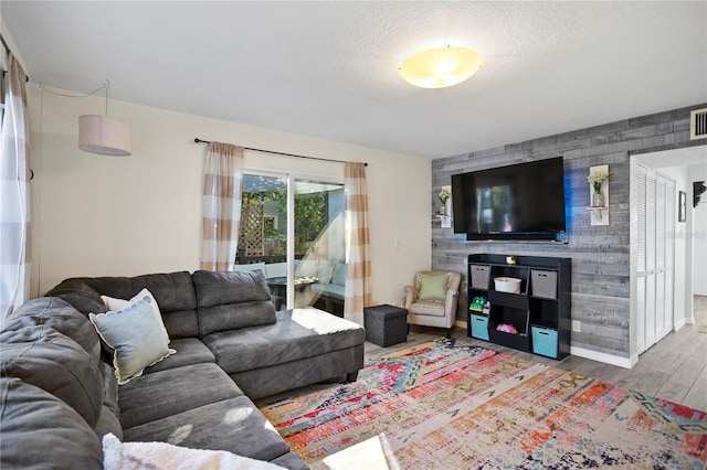 living room featuring visible vents, an accent wall, a textured ceiling, wood finished floors, and baseboards