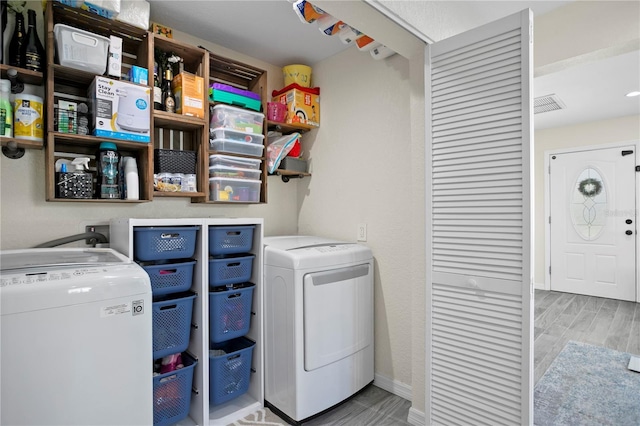 clothes washing area with laundry area, wood finished floors, washing machine and clothes dryer, and visible vents