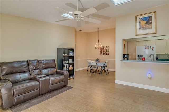 living room with lofted ceiling, baseboards, light wood finished floors, and ceiling fan with notable chandelier