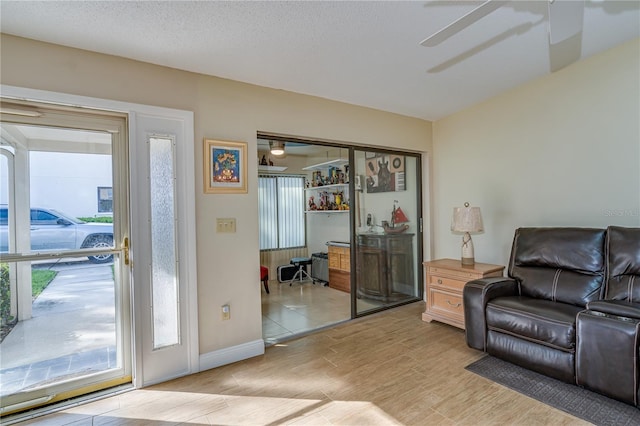 living area with light wood-style floors, plenty of natural light, ceiling fan, and a textured ceiling