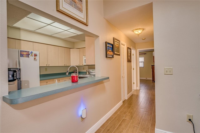 kitchen with white appliances, a sink, baseboards, cream cabinetry, and light wood-type flooring