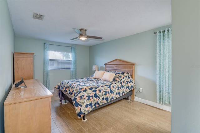 bedroom with a ceiling fan, light wood-type flooring, visible vents, and baseboards