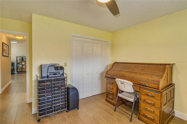 home office with light wood-style floors, a textured ceiling, baseboards, and a ceiling fan