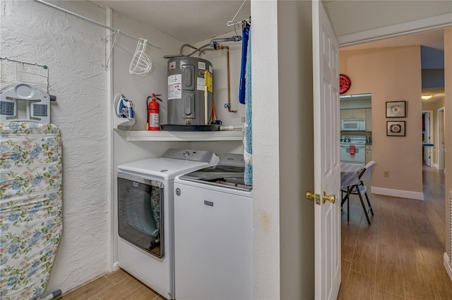 washroom featuring laundry area, separate washer and dryer, baseboards, water heater, and light wood-style floors