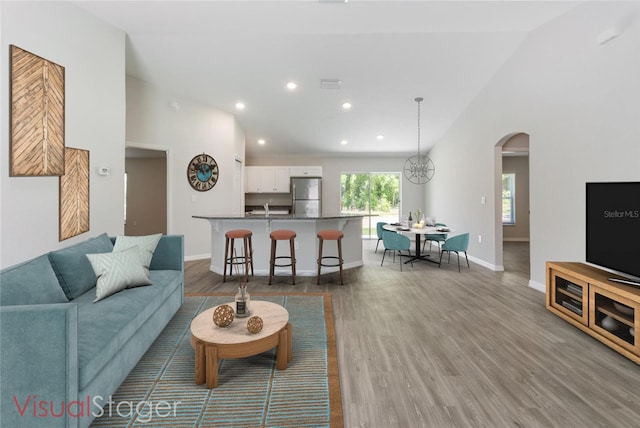 living room featuring high vaulted ceiling, baseboards, arched walkways, and wood finished floors