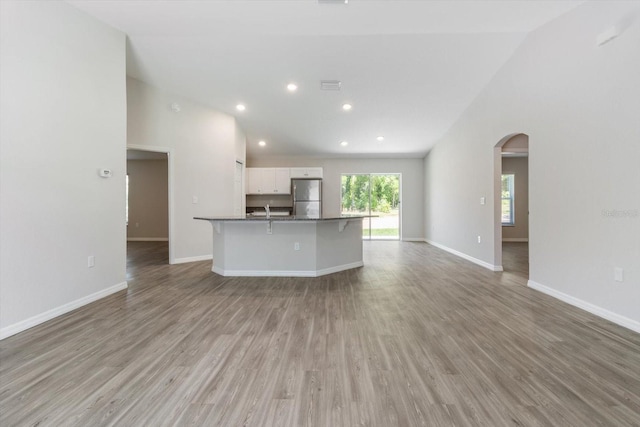 unfurnished living room featuring arched walkways, high vaulted ceiling, light wood-style flooring, recessed lighting, and baseboards