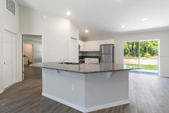 kitchen featuring visible vents, white cabinets, a breakfast bar area, freestanding refrigerator, and a sink