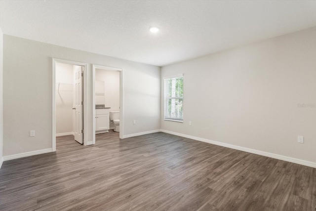 unfurnished bedroom with dark wood-type flooring, connected bathroom, and baseboards