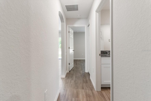 corridor with light wood-style floors, visible vents, a textured wall, and baseboards