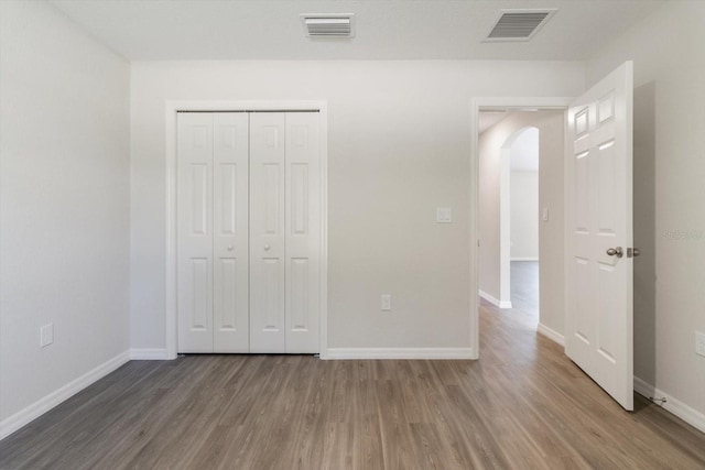 unfurnished bedroom with arched walkways, wood finished floors, visible vents, and baseboards