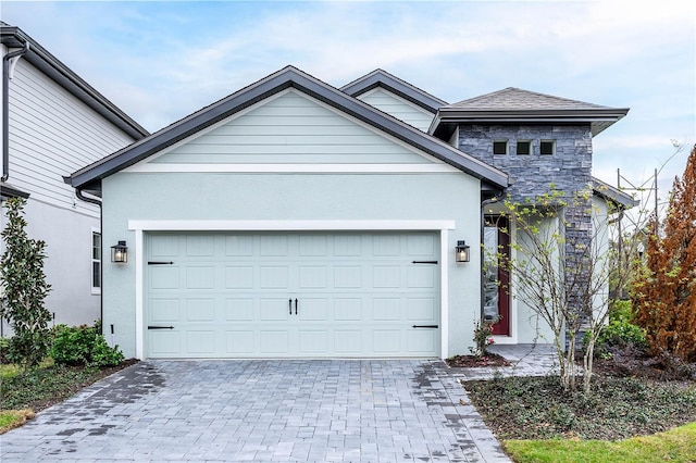 view of front of property featuring decorative driveway, stone siding, a garage, and stucco siding