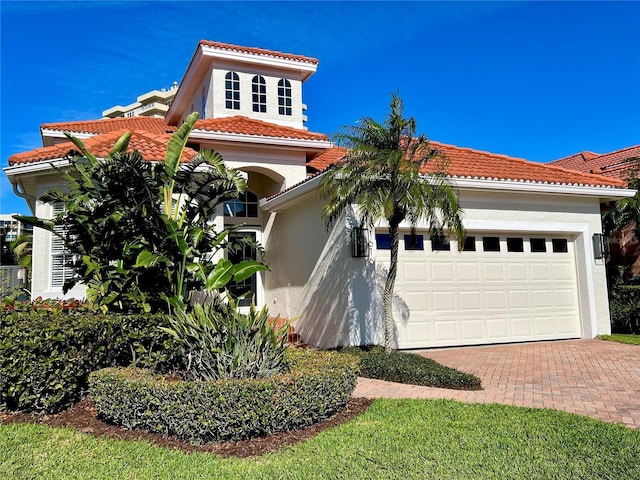 mediterranean / spanish home with decorative driveway, a tiled roof, an attached garage, and stucco siding