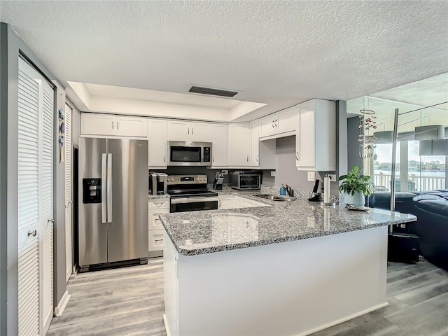 kitchen featuring stone countertops, stainless steel appliances, a peninsula, a sink, and visible vents