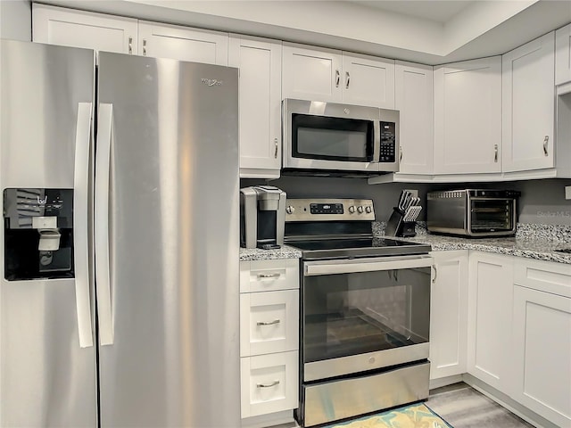 kitchen featuring stainless steel appliances, a toaster, white cabinets, and light stone counters