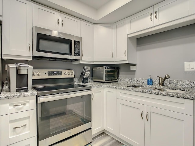 kitchen featuring stainless steel appliances, a toaster, white cabinets, and a sink