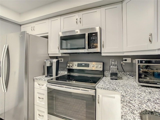 kitchen with white cabinets, a toaster, light stone counters, and stainless steel appliances