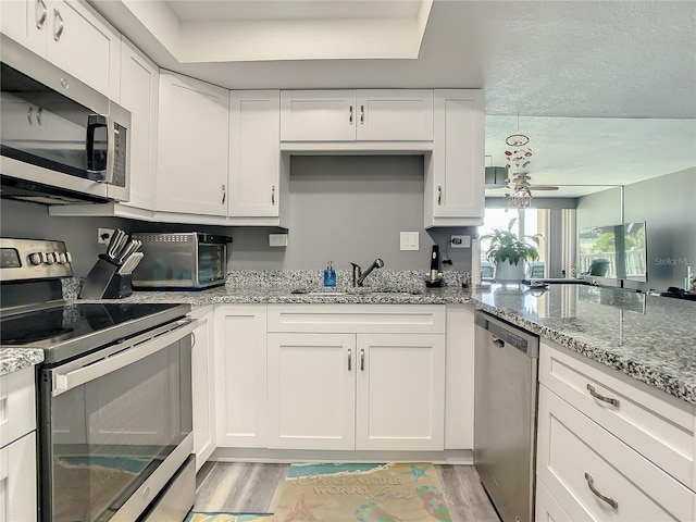 kitchen with stainless steel appliances, a sink, light stone countertops, and white cabinets