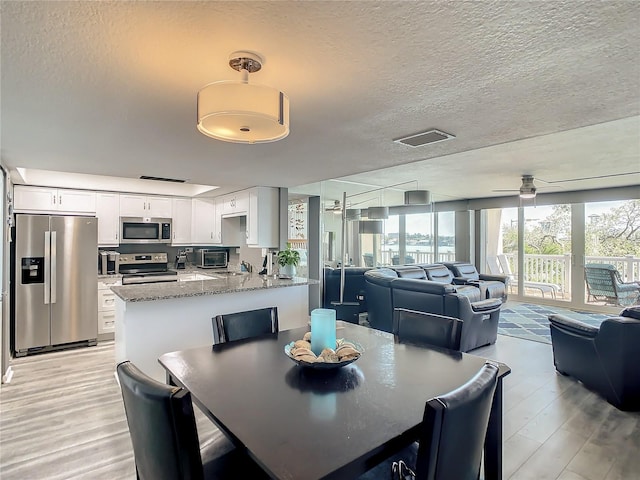 dining area with light wood finished floors, a ceiling fan, and a textured ceiling