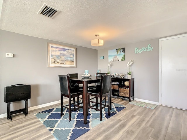 dining room with visible vents, a textured ceiling, baseboards, and wood finished floors