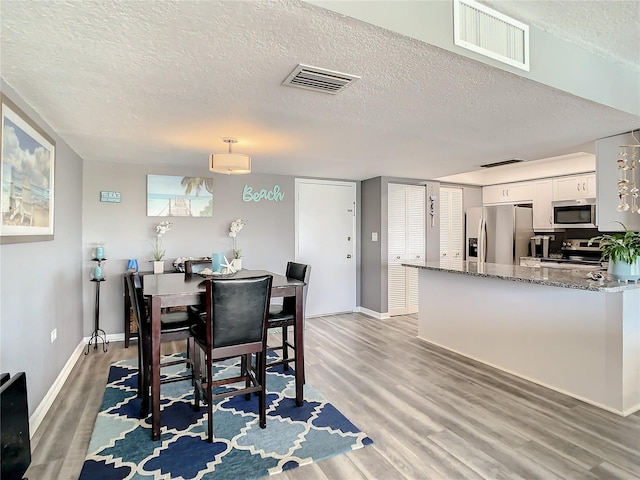 dining area with a textured ceiling, wood finished floors, visible vents, and baseboards