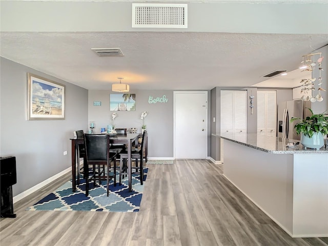 dining area featuring a textured ceiling, wood finished floors, visible vents, and baseboards