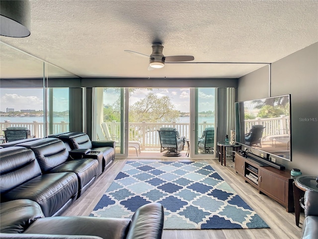 living area featuring light wood-style floors, a water view, a textured ceiling, and a ceiling fan