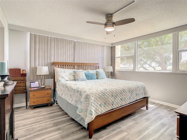 bedroom featuring a textured ceiling, multiple windows, baseboards, and wood finished floors