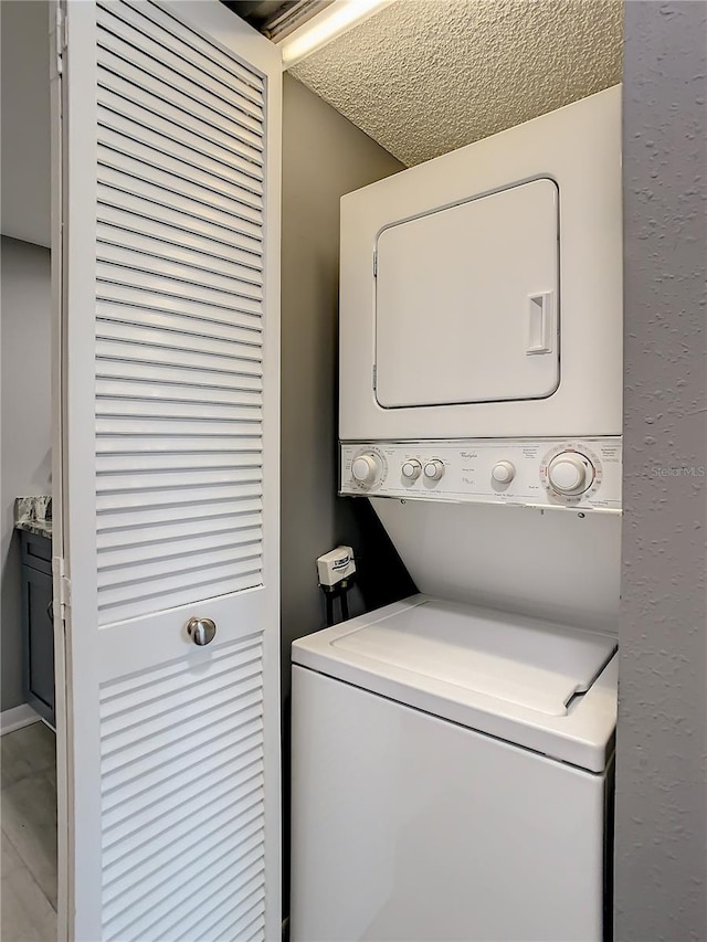 washroom with stacked washing maching and dryer, laundry area, and a textured ceiling