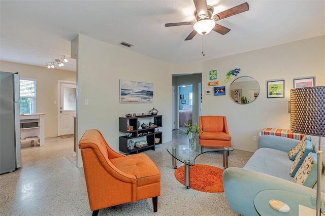 living area featuring light speckled floor, visible vents, and a ceiling fan