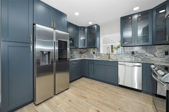 kitchen with light stone counters, wood finish floors, backsplash, appliances with stainless steel finishes, and a sink