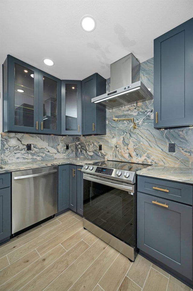 kitchen featuring stainless steel appliances, wood finish floors, wall chimney exhaust hood, and tasteful backsplash