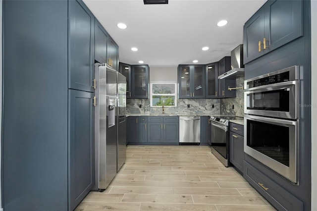 kitchen with stainless steel appliances, tasteful backsplash, wood tiled floor, a sink, and wall chimney exhaust hood